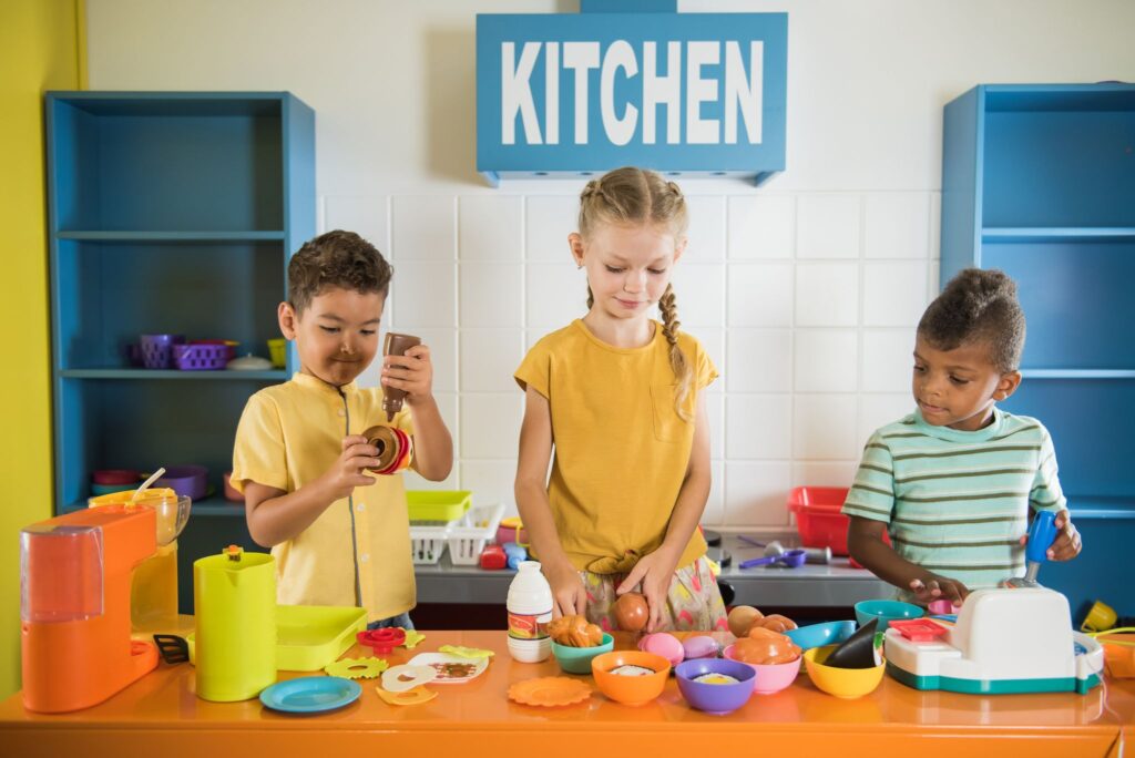 Kids playing with plastic food at daycare. Two boys and one girl playing in childrens room. Entertainment center and childrens game.