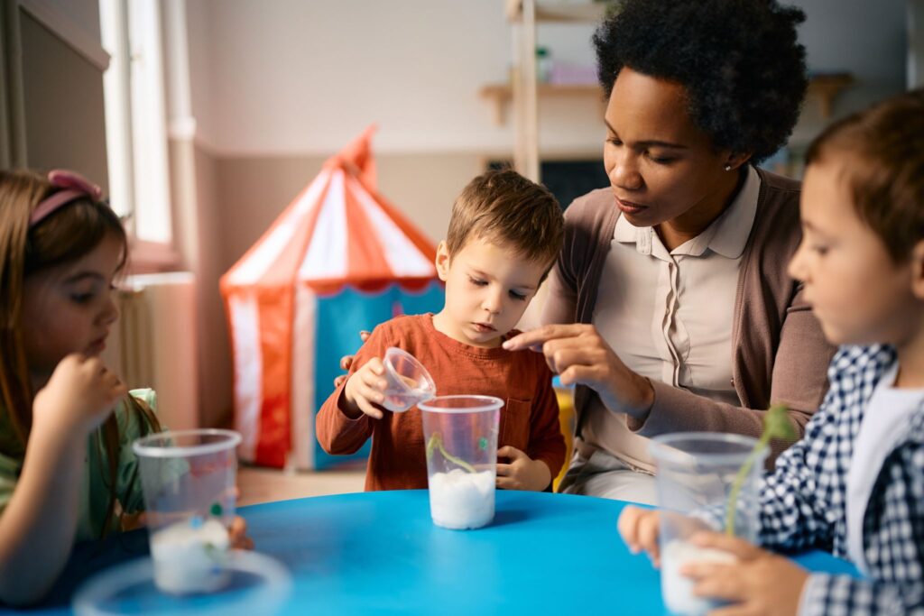 African American preschool teacher assisting kids with planting seeds during biology class.