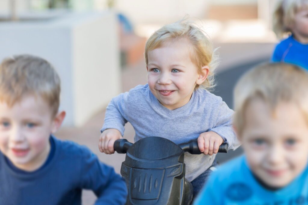 Boys at preschool racing push motorbikes in garden