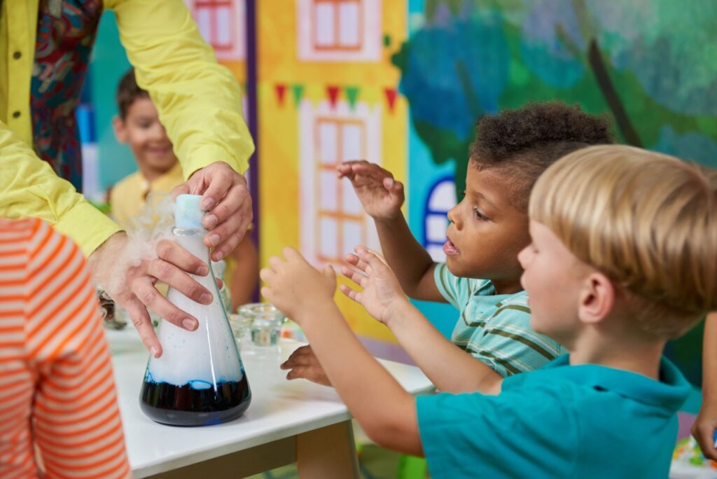 Happy kids at entertainment center. Children enjoying chemical show in playroom. Birthday party for kids.